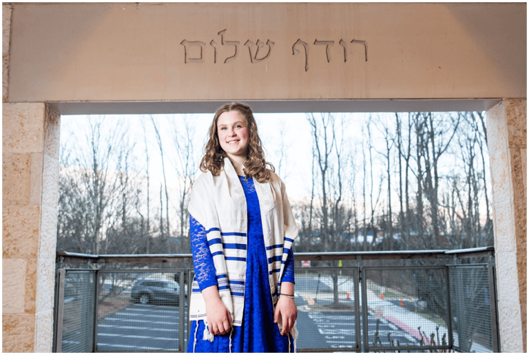 A student stands, smiling and wearing a tallit.