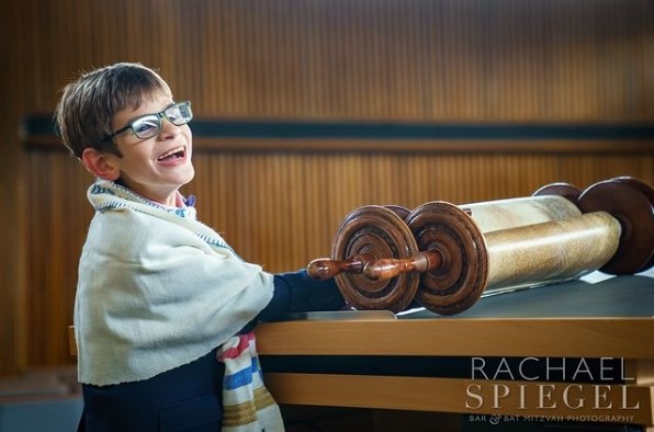 A student stands at the Torah, smiling.