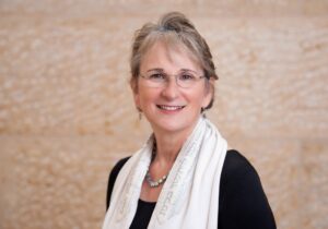 Portrait of Senior Rabbi Amy Schwartzman wearing a black dress and tallit
