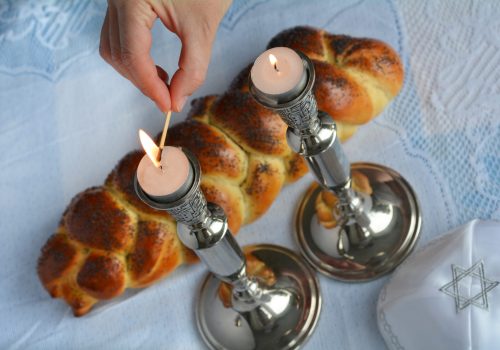 Shabbat eve table.Woman hand lit Shabbath candles with uncovered challah bread and kippah.